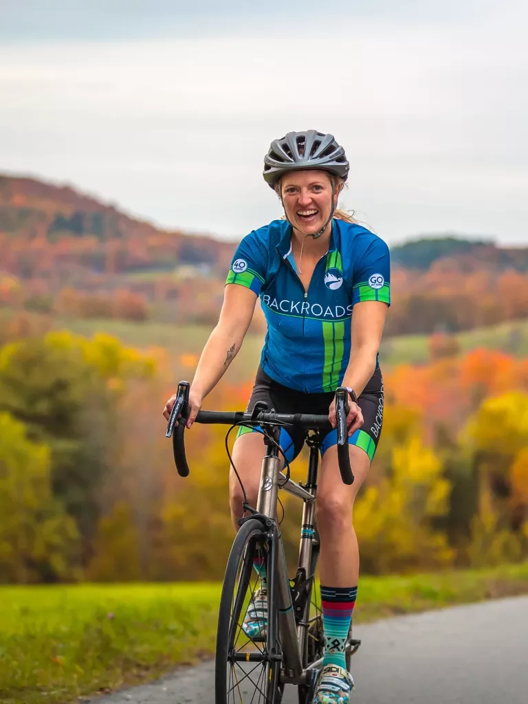 Guest cycling, smiling at camera, trees behind her.