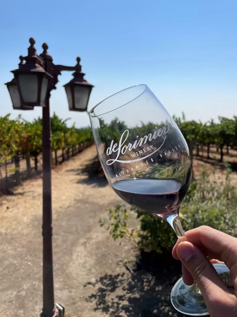 "de Lorimier" wine glass with vineyard and lamp post in background.