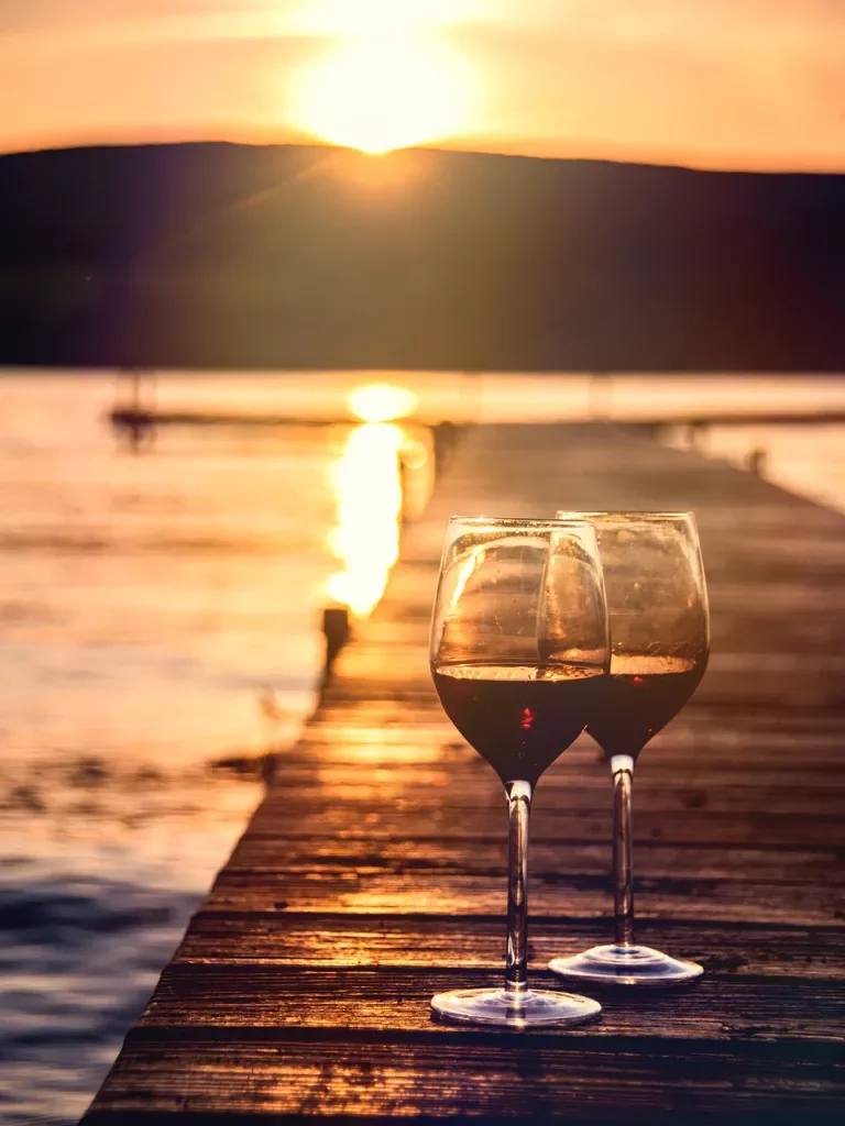 Two wine glasses sitting on pier, sunset in background.