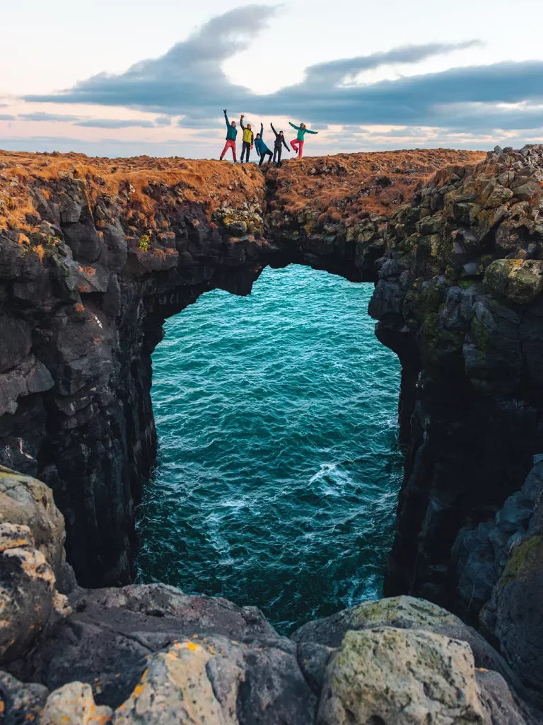 Guests posing on rock archway above ocean
