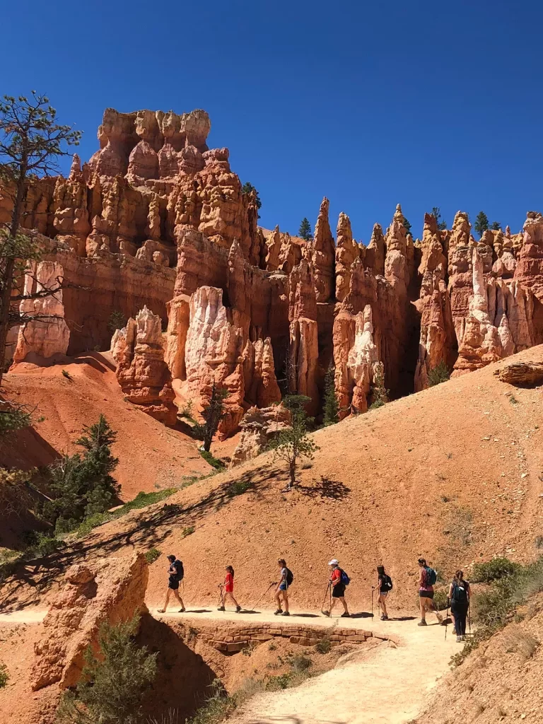 Guests hiking along orange rock trail, hoodoos behind them.