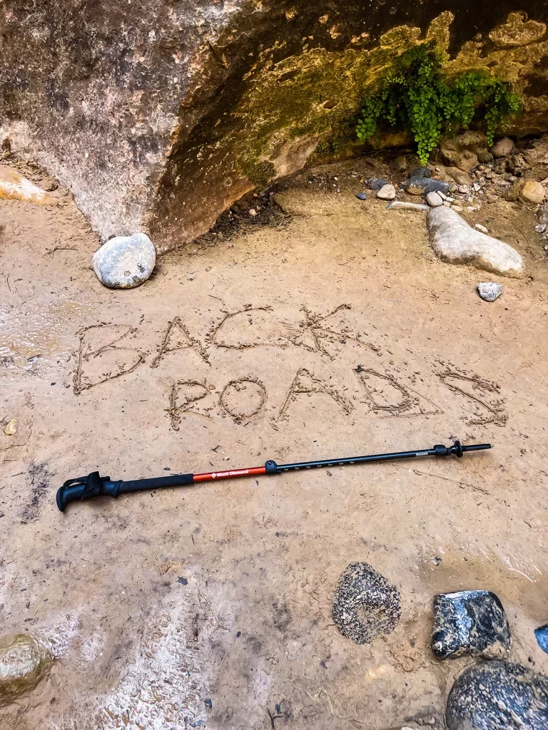 Shot of hiking pole on trail, "Backroads" etched into the mud above.