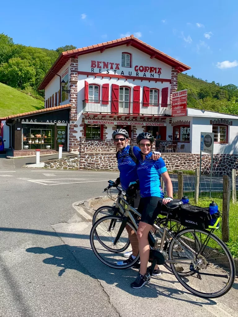 Two guests on bikes in front of "Benta Gorria", a red and white building.