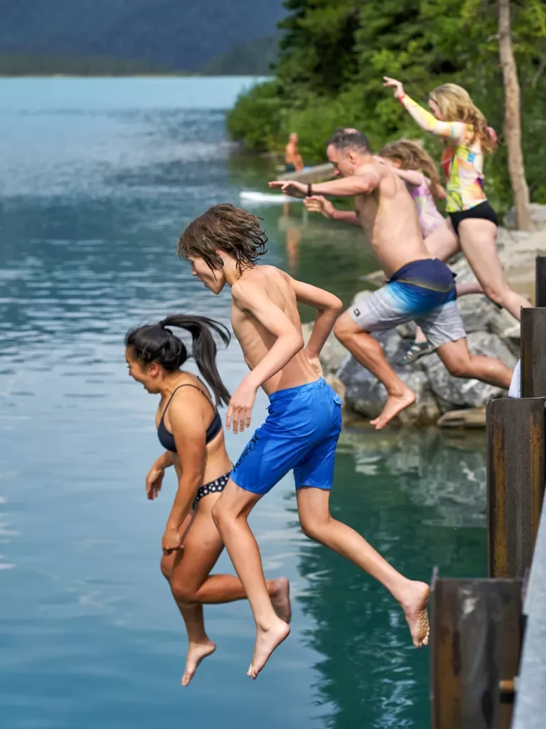 Group of guests jumping into lake from pier.