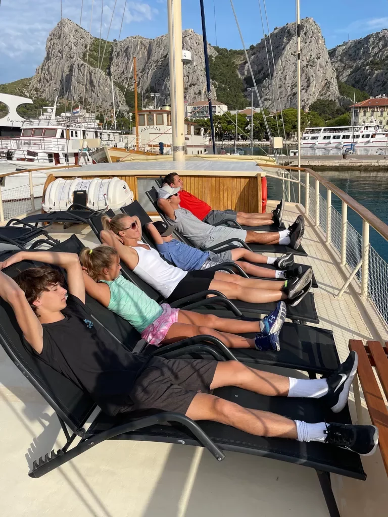 Guests reclining on boat deck, craggy cliffs in distance.