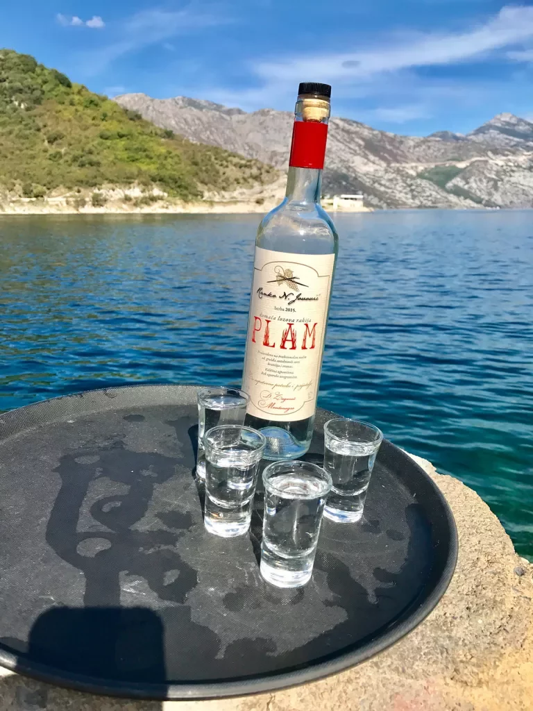 Platter with bottle and four shot glasses, river, hills behind it.