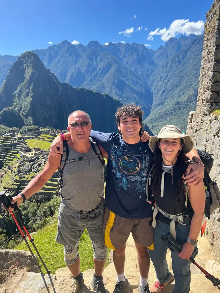Three guests with hiking poles posing, Machu Picchu behind them.