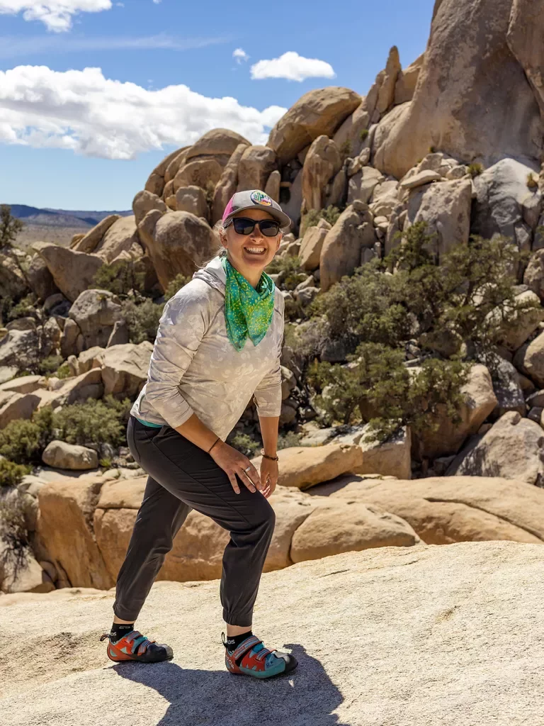 Guest hiking up desert boulder, craggy sandstone rocks in background.