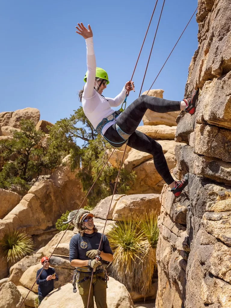 Three guests rock climbing, one is waving to the camera.