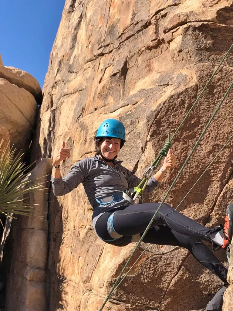 Guest climbing on the side of a boulder, giving thumbs up.