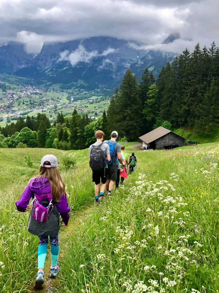 Group of guests hiking towards small rocky shack, large valley town and mountain range in distance.