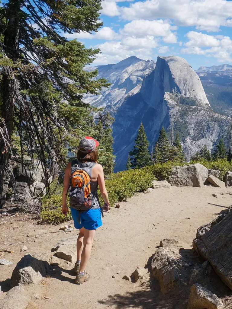Guest walking on mountain trail, Half Dome in distance.