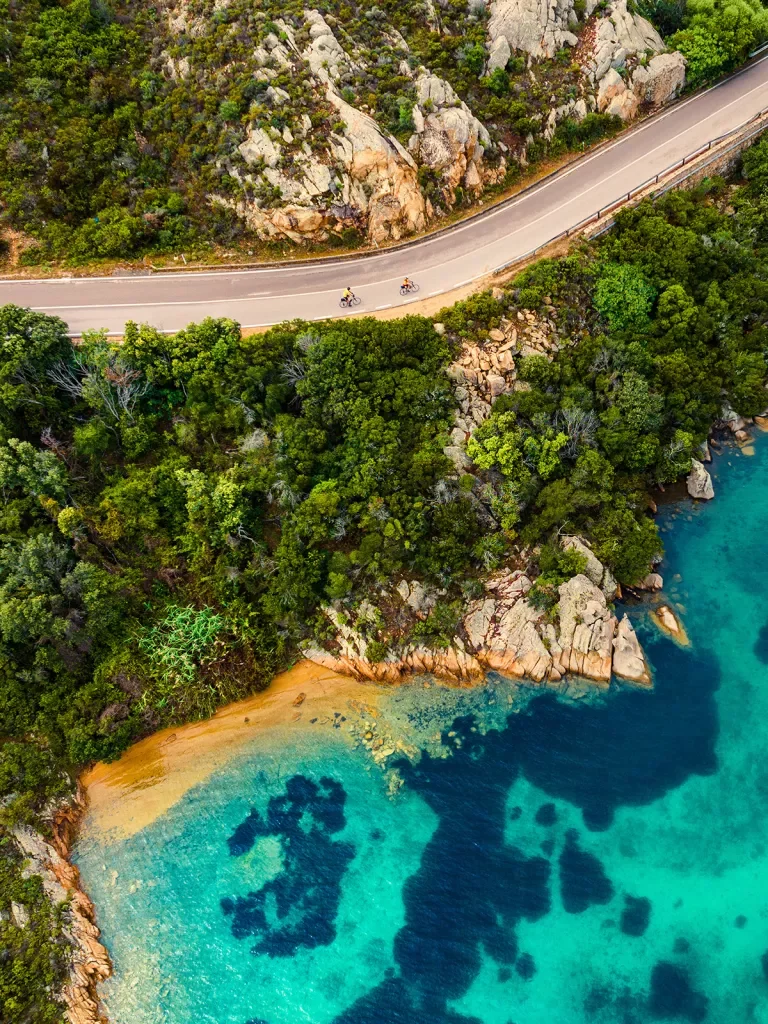 Overhead shot of guests cycling on coastal road, small beach, blue water.