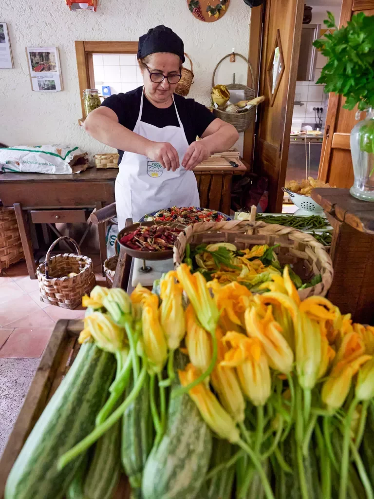 Local chef preparing food, zucchini + blossoms in foreground. 