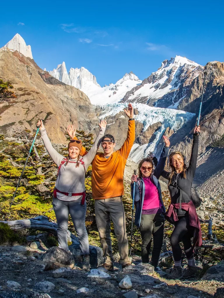 Four guests posing, hand above thier heads, large snowy peaks behind them.