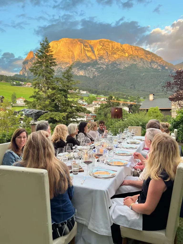 Group of guests at dinner table, sunset-kissed mountains in distance.