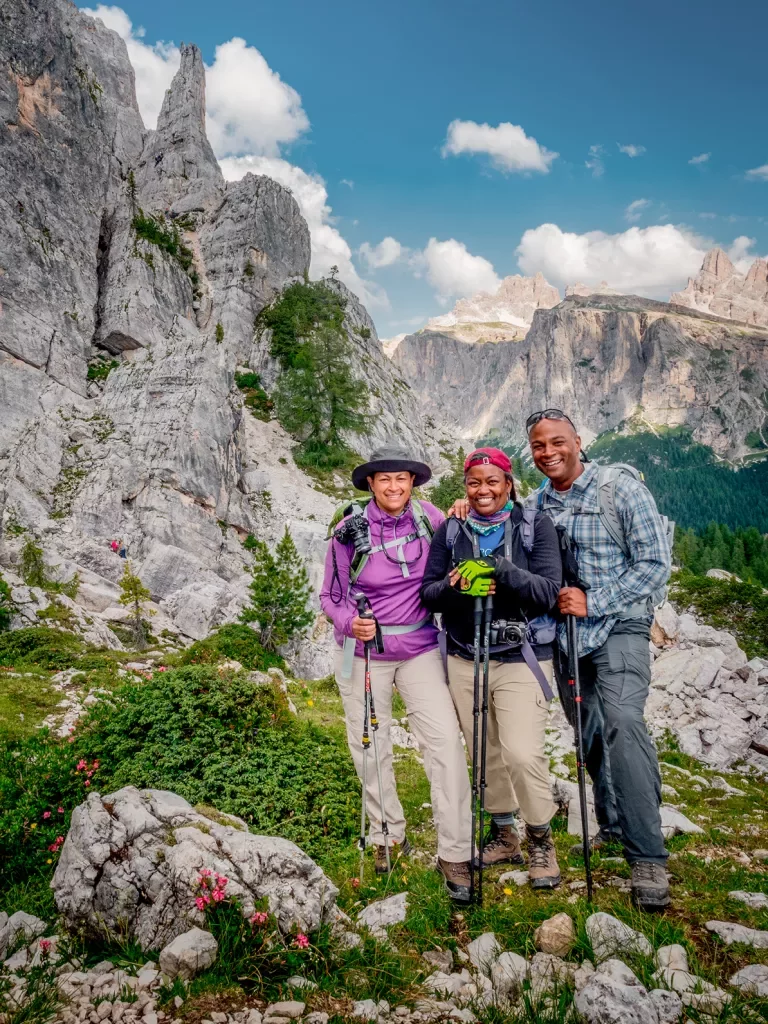 Three guests in hiking gear, craggy cliffside to their right.