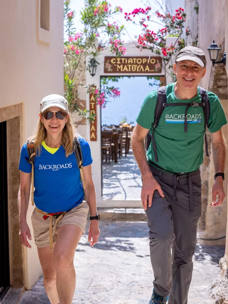 Two guests walking down narrow Grecian alleyway towards camera.