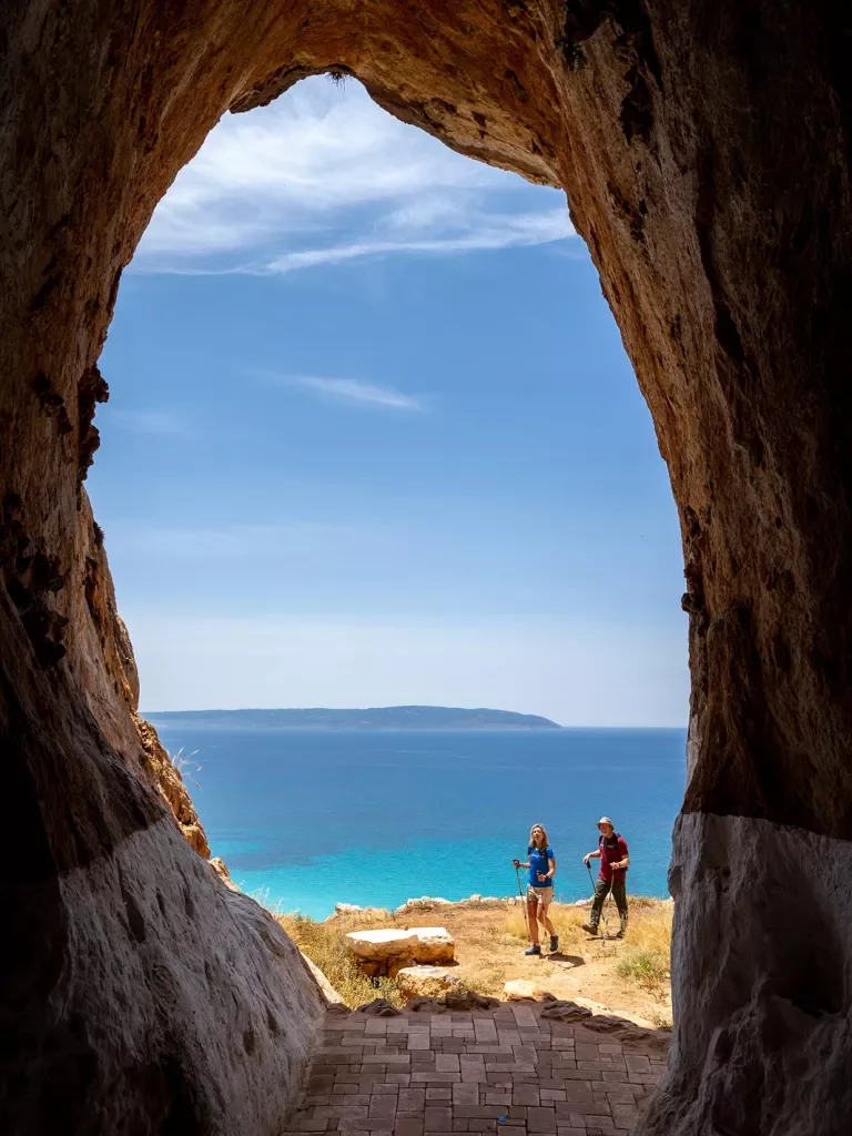 POV shot inside large cave, looking out towards two guests, ocean view.