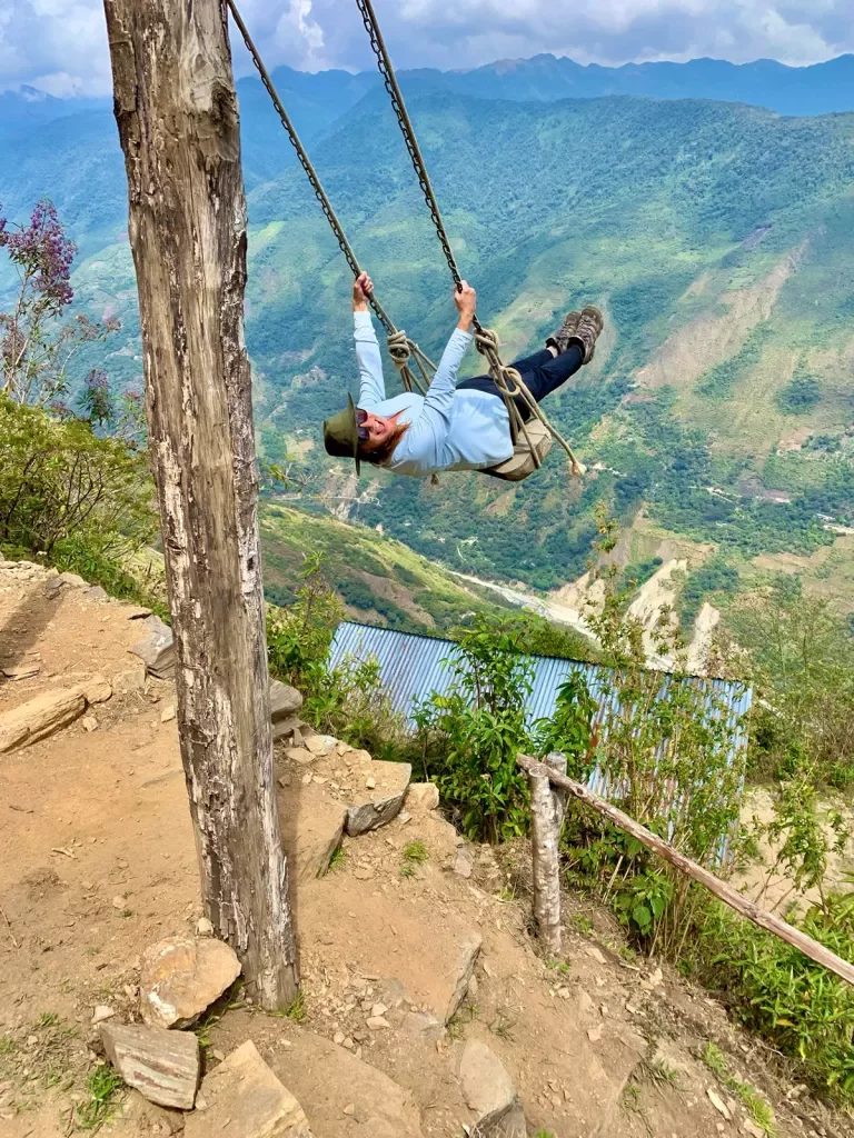 Guest on cliffside swing, overlooking large drop.