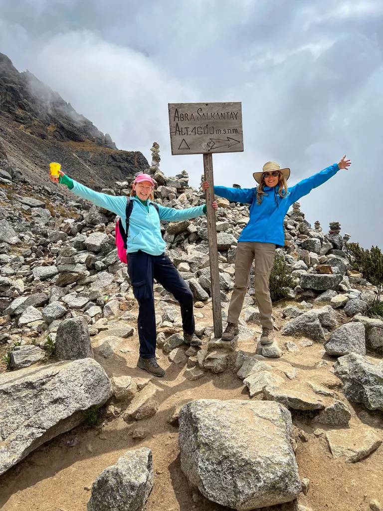 Two guests with "ABRA SALKANTAY" sign, clouds and cliff behind them.