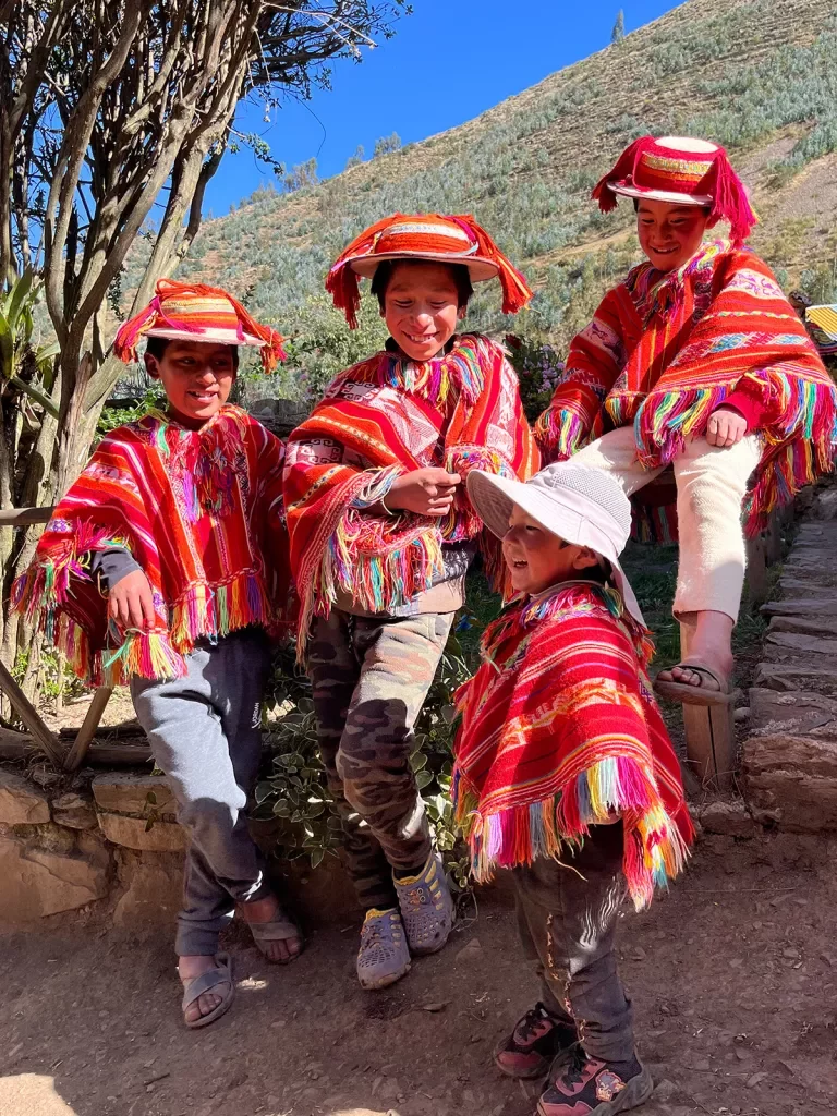 Four young locals in colorful, traditional attire. Leaning on stone wall.