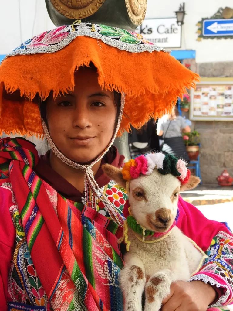 Local in colorful garb with sheep, looking at camera.