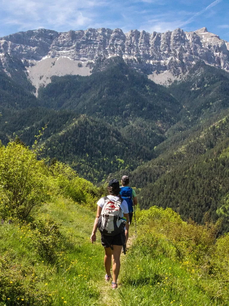 Two guests on mountain trail, walking towards large range.