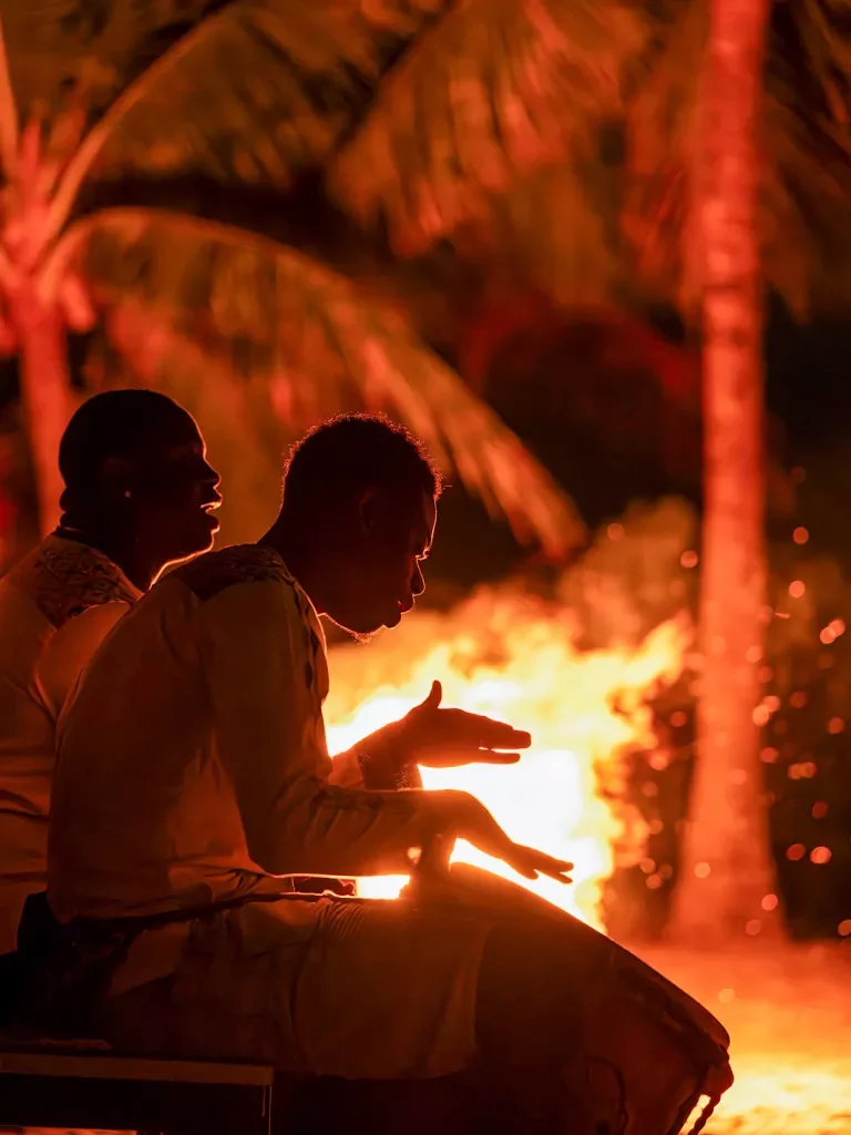Two men playing bongos around a campfire