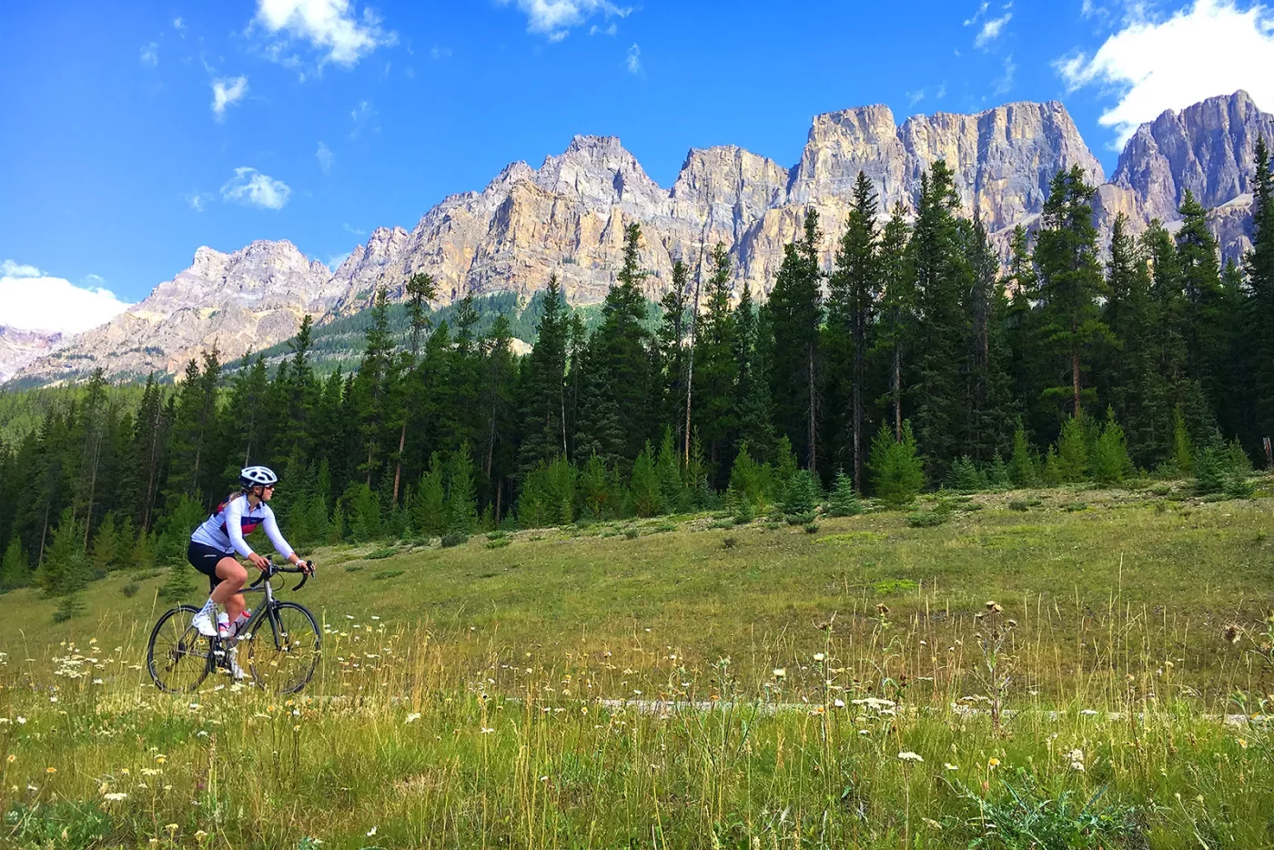 Guest cycling through grassy meadow, large, craggy mountain peaks in background.