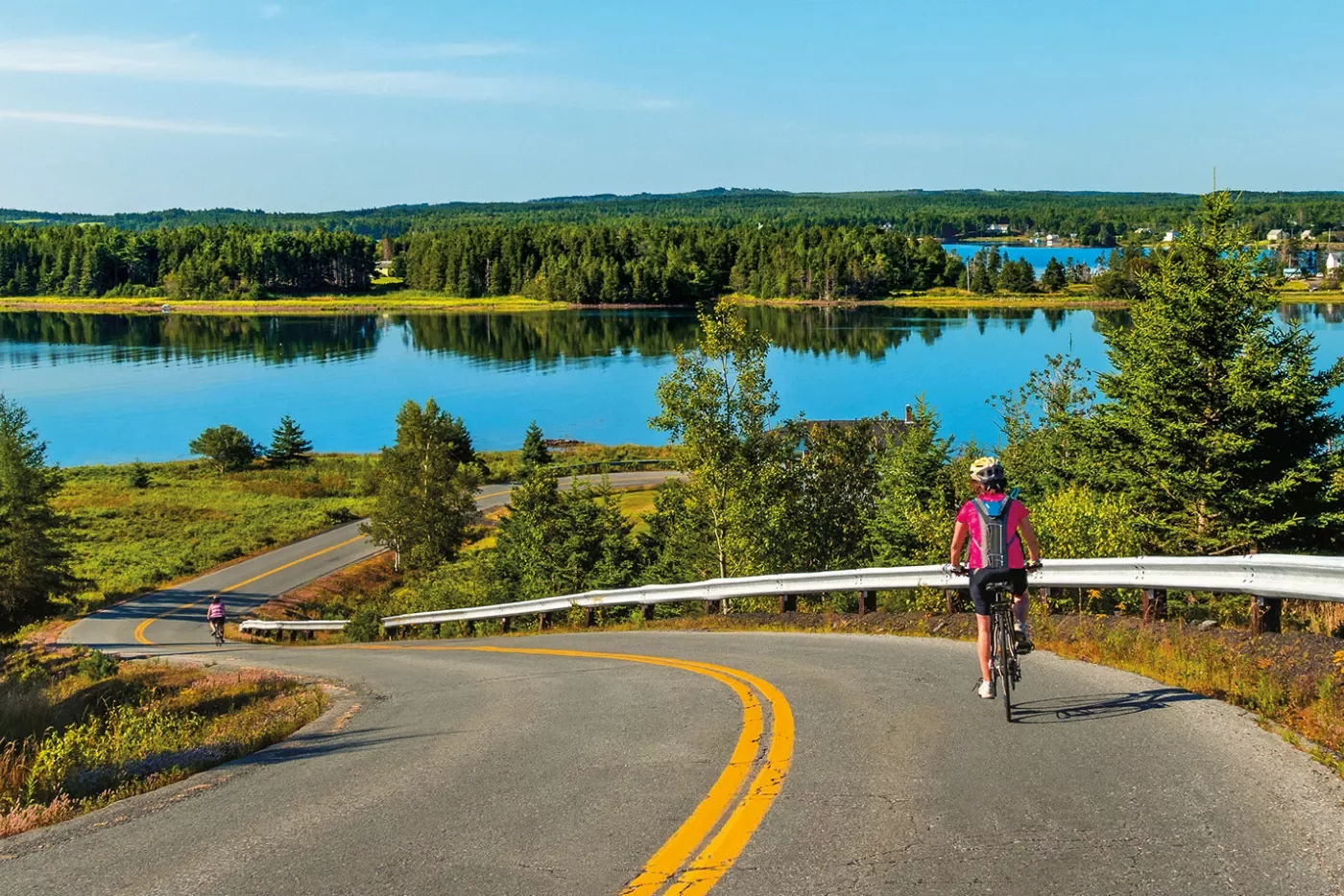 Guest cycling down road, large lake or river in background.