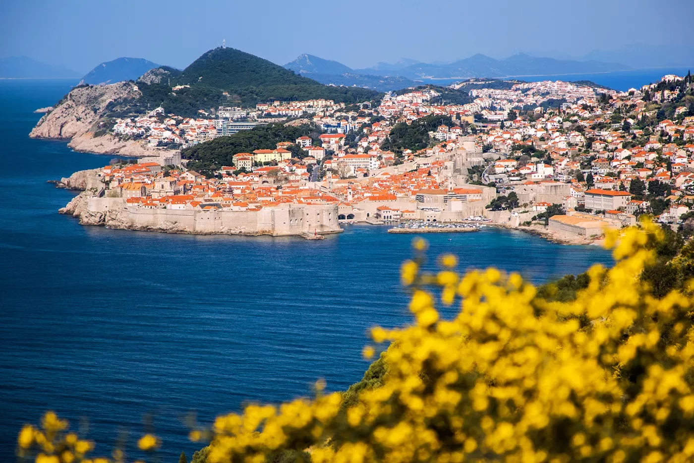 Wide shot of Dubrovnik coastline, blue ocean, white and tan houses.