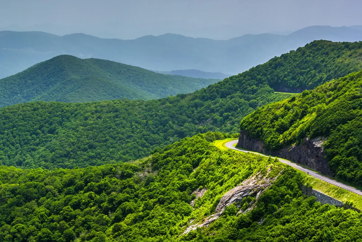 Wide shot of mountain road, overlooking large forested mountains.
