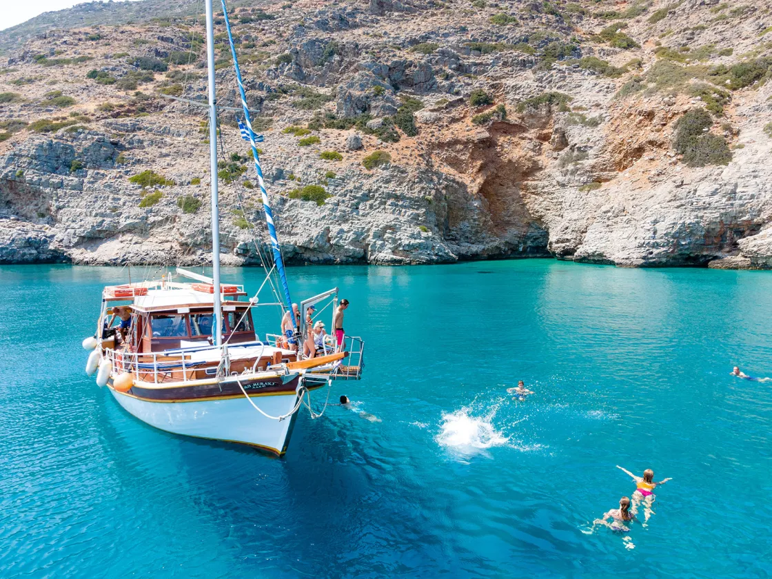 Guests near and on boat, swimming, relaxing, rocky coast nearby.